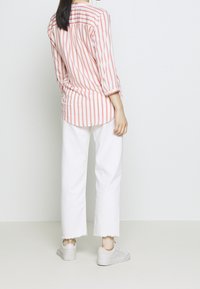Blusa leggera a righe rosa e bianche con maniche a tre quarti, abbinata a jeans bianchi a vita alta e sneakers chiare.