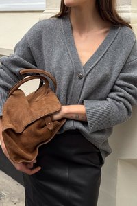 Grauer Strick-Cardigan mit V-Ausschnitt und Knopfschluss. Das Modell hält eine braune Wildleder-Handtasche, die von einem schwarzen Lederrock ergänzt wird.