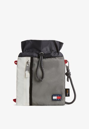 Mała sakiewka ze ściągaczem, czarnym górnym paskiem, białym bocznym panelem z zamkiem błyskawicznym, szarą siateczkową przednią częścią oraz naszywką z logo Tommy Jeans w prawym dolnym rogu.