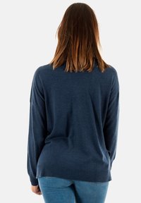 Mörkblå stickad tröja med långa ärmar, rundad halsringning och ribbad fåll. Mjuk textur; avslappnad passform. Bärs med ljusblå jeans.