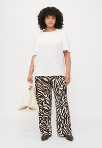 White short-sleeve top with a round neckline, paired with wide-leg pants featuring a black and brown zebra stripe pattern, carrying a cream bag.