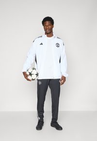 Athletic outfit featuring a white tracksuit jacket with black accents, gray pants with white stripes, and a soccer ball.