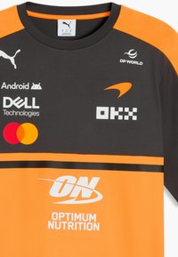 Camiseta deportiva de manga corta en negro y naranja con logotipos de patrocinadores que incluyen Puma, Android, Dell, Mastercard, DP World, OKX y Optimum Nutrition.