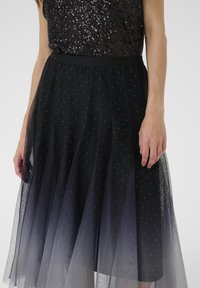 Čierna tylová sukňa s A-liniovou siluetou, zdobená rozptýlenými striebornými bodkami, s pevným pásom a vrstvenou textúrou.