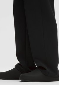 Zwarte, zachte materiaal schoenen met een ronde neus, gecombineerd met losse zwarte broeken met geknipte zoom en een gladde textuur.