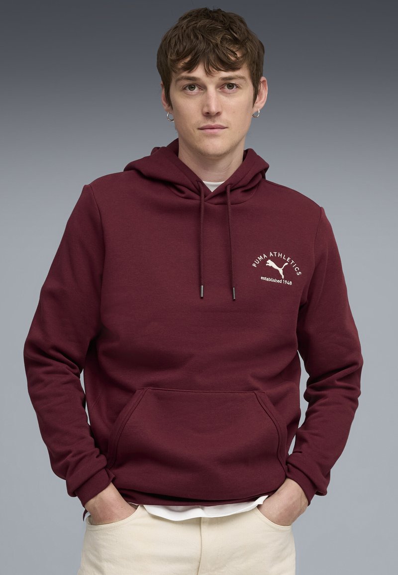 Bordeaux hoodie lavet af bomuldsblanding, med en kængurulomme, snorhætte og hvidt trykt logo på brystet.