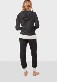 Sudadera negra con un dobladillo acanalado blanco, combinada con joggers negros a juego que cuentan con puños blancos. Material suave de punto, ajuste informal.