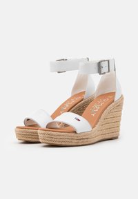 Bílé klínové sandály s podešví v espadrillovém stylu z juta, s širokým předním páskem a nastavitelným páskem kolem kotníku s kovovou sponou.
