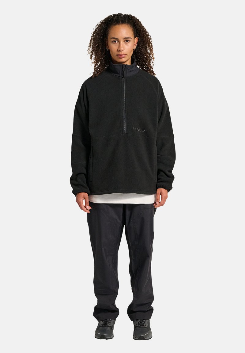 Zwarte fleece pullover met een hoge kraag en een halve ritssluiting, voorzien van een geborduurd "HALO" logo. Gecombineerd met losse zwarte broek en schoenen.