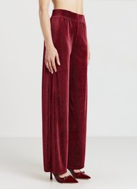 Rote Samt-Hose mit weitem Bein und strukturiertem Rautenmuster, ausgestattet mit einem elastischen Bund. Kombiniert mit spitzen roten High Heels als Kontrast.