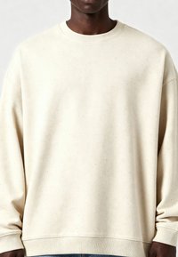 Kreminės spalvos medvilninis džemperis su tekstūruotu, dėmėtu paviršiumi. Turi apvalią kaklo iškirptę ir marškinius su raukšlėmis, sukurtas su laisvu siluetu.