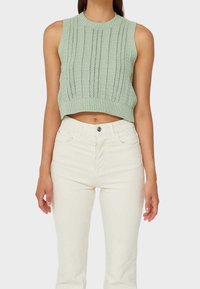 Mint green knitted crop top with a ribbed hem and vertical patterns. Paired with high-waisted white jeans.