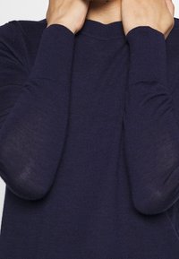 Marineblau gestrickter Pullover mit langen Ärmeln und Rundhalsausschnitt. Weiche Textur mit gerippten Bündchen und subtilen Nahtdetails entlang der Schultern.