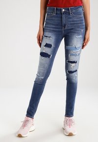 Svetle modré roztrhané skinny džíny s několika poškozenými místy a vysokým pasem. Spárovány se světle růžovými sportovními botami.