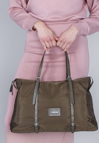 Olijfgroene nylon draagtas met zilveren hardware, dubbele handvatten bovenaan en een rechthoekig logo-opdruk, met een gladde textuur en gestructureerd ontwerp.