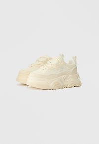 Klumpete joggesko i lys gul, med teksturert mesh og semsket overdel, mønstret såle, runde snører, og løkke-heelskinn.