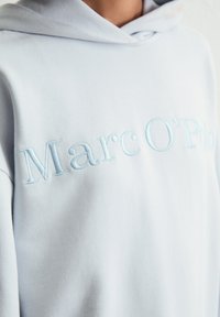 Lichtblauwe pullover hoodie gemaakt van zachte stof, met geborduurde "Marc O'Polo" tekst in een iets donkerder blauw op de voorkant.