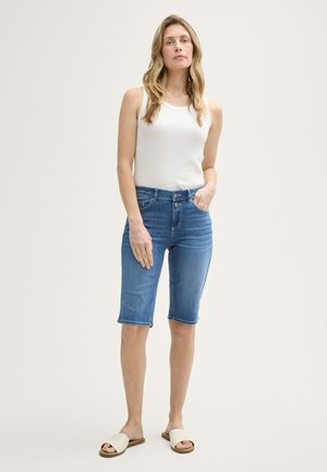 Shorts de mezclilla de color azul medio, de largo a la rodilla y con un diseño ajustado. Combinados con una camiseta sin mangas blanca y sandalias deslizantes beige. Textura suave, sin patrones visibles.