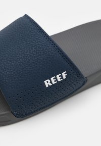 Sandali blu scuro con una fascetta superiore strutturata dotata di perforazioni e suola in gomma grigia, contrassegnati con il nome del marchio "REEF."