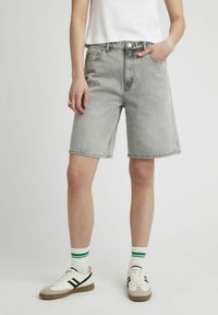 Shorts en denim gris à coupe décontractée, présentant un design classique à cinq poches et un ourlet piqué. Associés à des chaussures sportives et des chaussettes rayées.