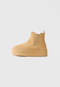 Botte cheville en daim tan avec semelle épaisse, panneaux latéraux élastiques et languette, présentée de l'extérieur sur un fond uni.