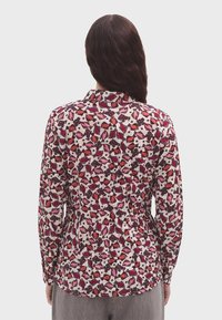 Blusa de manga larga con un estampado floral en rosa, rojo y blanco, con cuello y detalles de botones, fabricada en una tela ligera.