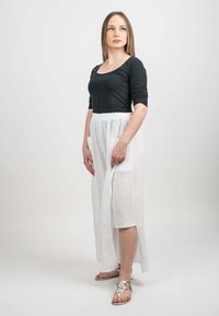 Haut noir à manches longues, jupe maxi en lin blanc avec taille élastique et poches, sandales plates argentées avec accents décoratifs.