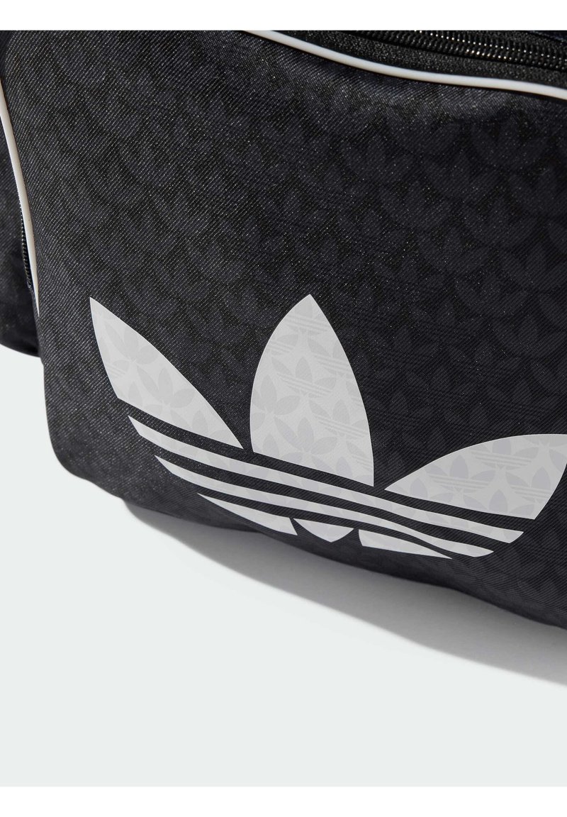 Bolsa de tela negra con un gran logo trefoil blanco de Adidas y rayas horizontales, con un patrón texturizado en el fondo.