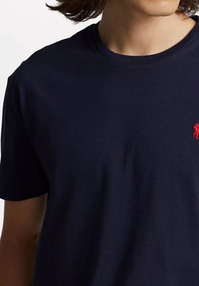 T-shirt in cotone blu navy con scollatura a girocollo, maniche corte e un piccolo logo rosso sul petto. Texture liscia, vestibilità standard.