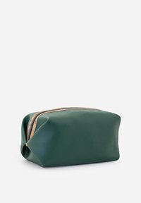 Portapenne verde in pelle con chiusura a zip. Superficie morbida e testurizzata, forma arrotondata e design minimalista. Dettagli della zip color beige.