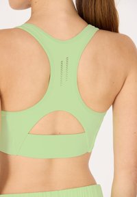 Grön sport-bh med racerback-design, utskärningar och små vertikala ventilationslinjer på ryggen. Slät yta med elastiskt tyg.