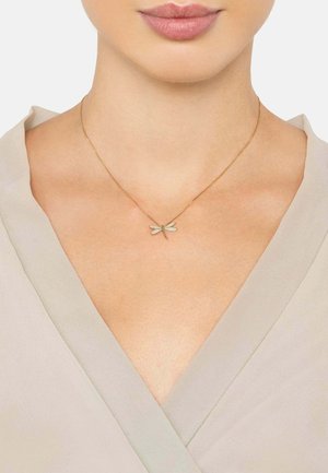Gold necklace featuring a dragonfly pendant adorned with clear stones, displayed on a model wearing a light beige top.