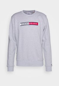 Šedá mikina z bavlněné směsi s kulatým výstřihem, dlouhými rukávy a horizontálním logem "TOMMY JEANS" přes hrudník v tmavě modré a červené barvě.