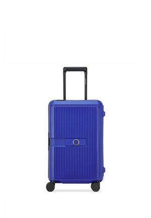 Maleta rígida azul con estrías verticales, cuatro ruedas negras, asa negra retráctil y correa horizontal central con detalle circular.