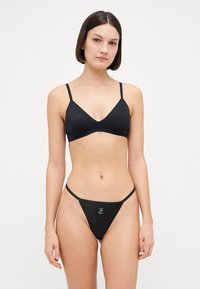 Zwart zwemset bestaande uit een triangletop en een dunne strap thong. Glad textuur met minimale hardware en een klein logo-detail.
