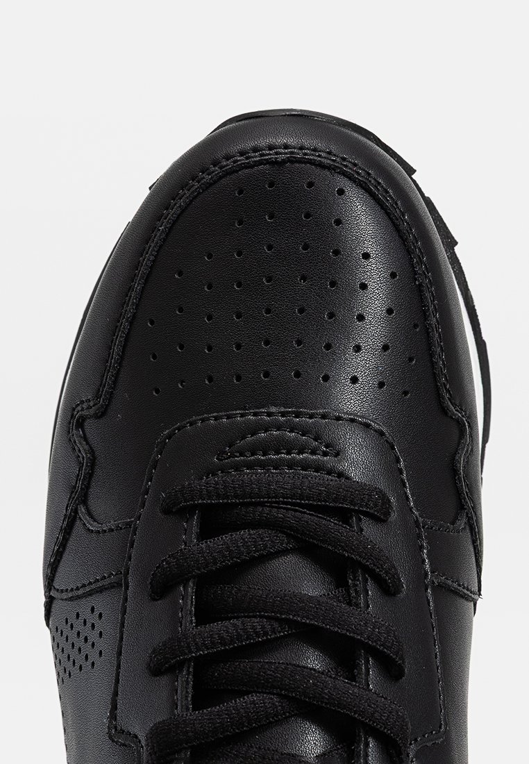 Sneaker in pelle nera con zona della punta perforata, lacci neri piatti e collarino imbottito. Presenta una suola bianca e dettagli di cucitura minimali.