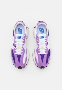 Paire de baskets New Balance blanches et violettes avec des lacets blancs, un logo bleu sur la languette et une semelle extérieure noire, vue de dessus.