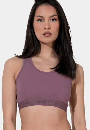 Donna che indossa un top sportivo malva con il marchio "yentia", capelli lisci e scuri, espressione neutra, su uno sfondo chiaro e uniforme.