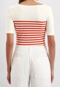 Top a rayas con base crema y franjas horizontales rojas. Tejido de punto suave, con mangas cortas y un escote amplio.