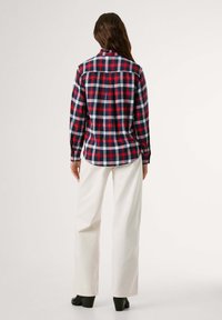 Κόκκινο, ναυτικό μπλε και λευκό πουκάμισο καρο φλις με μακριά μανίκια και στρογγυλή κόψη, φορεμένο με λευκά παντελόνια φαρδιά και μαύρες πλατφόρμες με τακούνι.