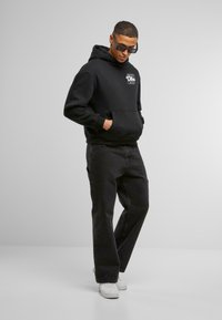 Felpa nera in cotone con tasca frontale e dettaglio grafico bianco. Abbinata a pantaloni neri e sneaker bianche. Design streetwear classico.