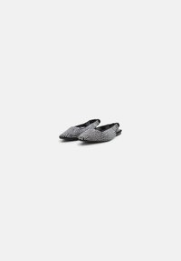 Zapatos negros de tacón tipo slingback con puntera afilada, adornados con tachuelas plateadas, con una superficie texturizada y suela plana.