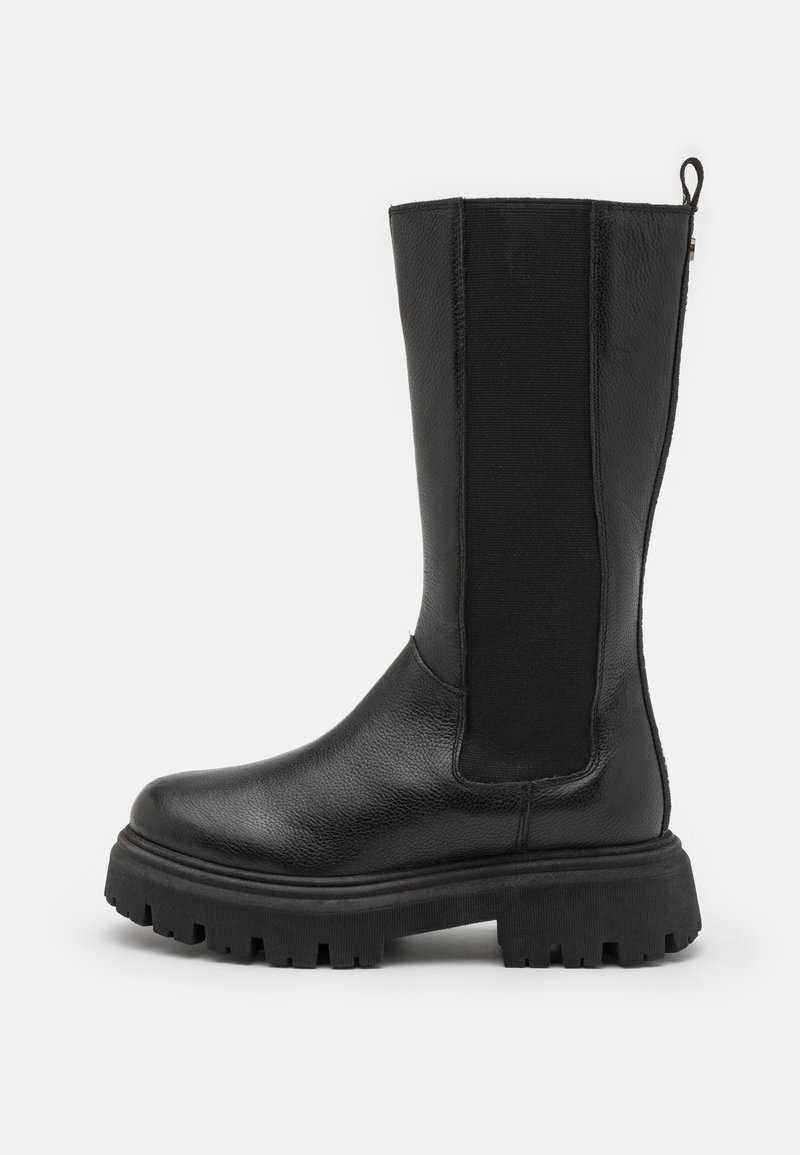 Botte en cuir noire mi-mollet avec semelle épaisse à crampons et panneau latéral élastique pour un enfilage facile, sur fond blanc.