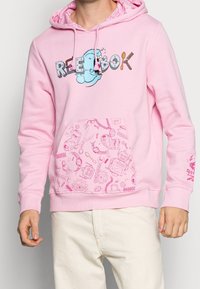 Rosa hoodie med ett grafiskt tryck av en karaktär och texten "REEBOK." Har en mönstrad ficka, dragsnören och ribbade ärmslut.