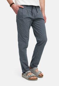 Pantalons légers rayés bleu et blanc avec une taille élastique et un cordon de serrage, dotés de poches latérales et associés à des sandales grises.