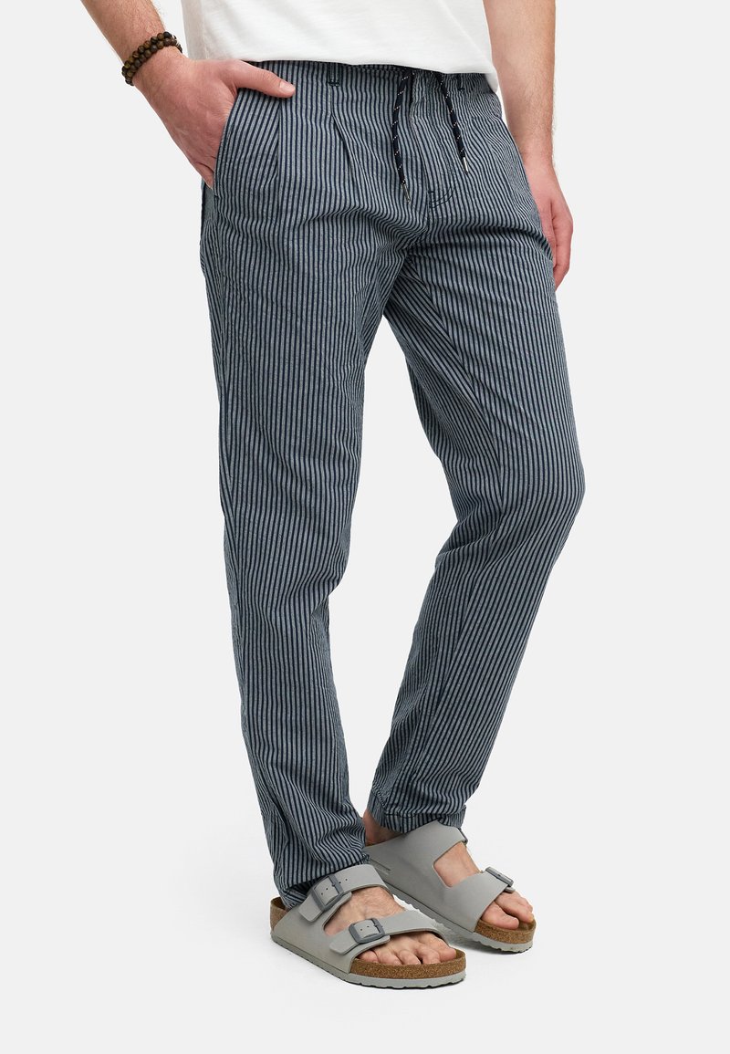 Pantalons légers rayés bleu et blanc avec une taille élastique et un cordon de serrage, dotés de poches latérales et associés à des sandales grises.