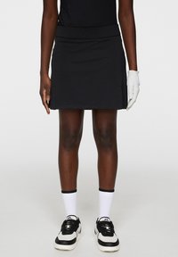 Svart golfkjol med bred midja, slim fit och sidofickor, tillsammans med vita korta strumpor och svart-vita sneakers.