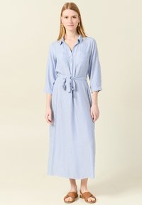 Abito camicia midi a righe blu e bianche con maniche lunghe, chiusura a bottoni e cintura annodata in vita. Presenta una vestibilità comoda e una morbida texture del tessuto.