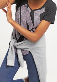 Svart och grå grafisk t-shirt med bold randdesign, ihopparad med en ljusgrå sweatshirt knuten runt midjan. Blå denimjeans.