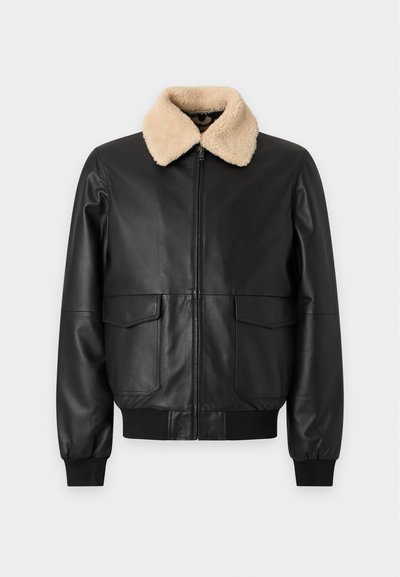 Veste en cuir noire avec col en agneau beige, fermeture éclair devant, deux poches à rabat, poignets et ourlet côtelés.